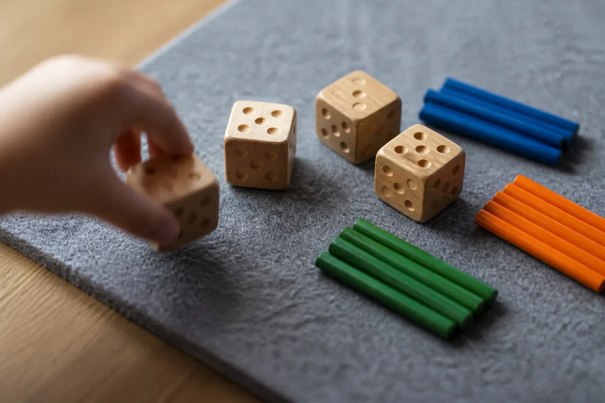 Cubes de bois marqués de points et petites baguettes colorées disposés sur un tapis de feutre gris, lumière latérale douce