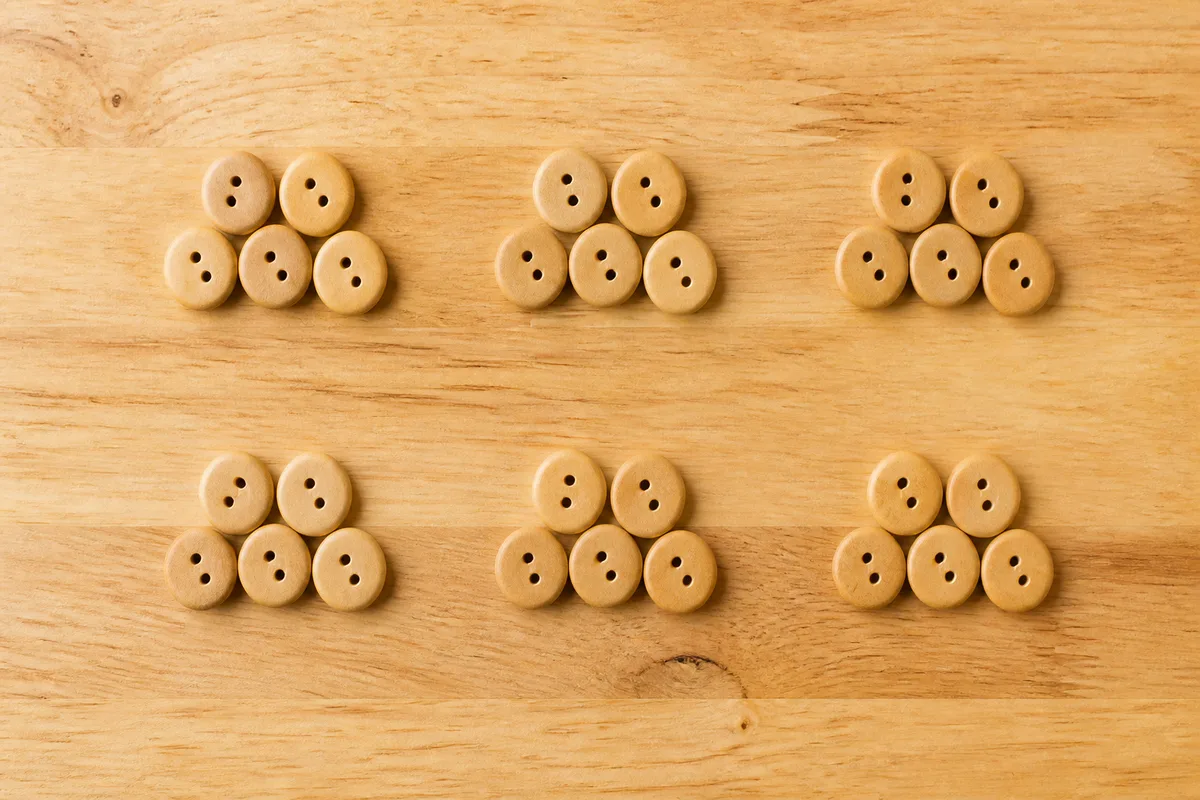 Petits boutons en bois répartis en plusieurs tas égaux sur un plateau de table en bois clair