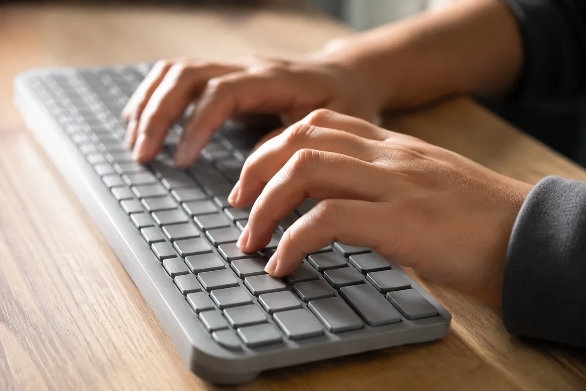 Mains d’adolescent en gros plan sur les touches d’un clavier posé sur un bureau en bois clair